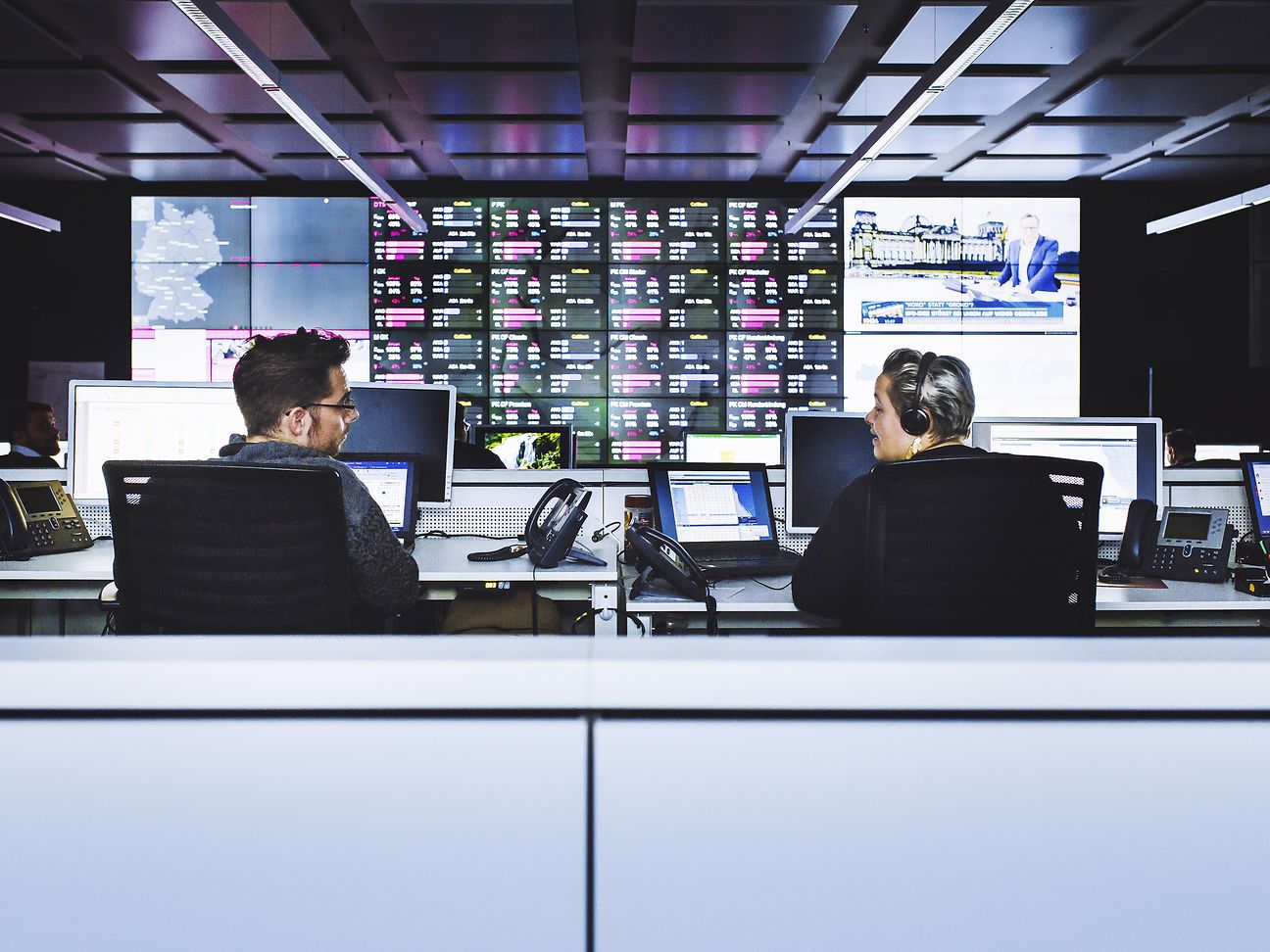 A male and female colleague, sitting at their respective work desks.