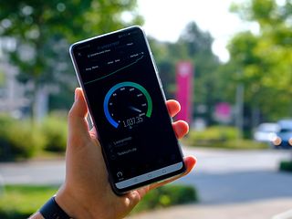 Blurred background, with a Telekom employee holding a smartphone, displaying a 5G network speed test.