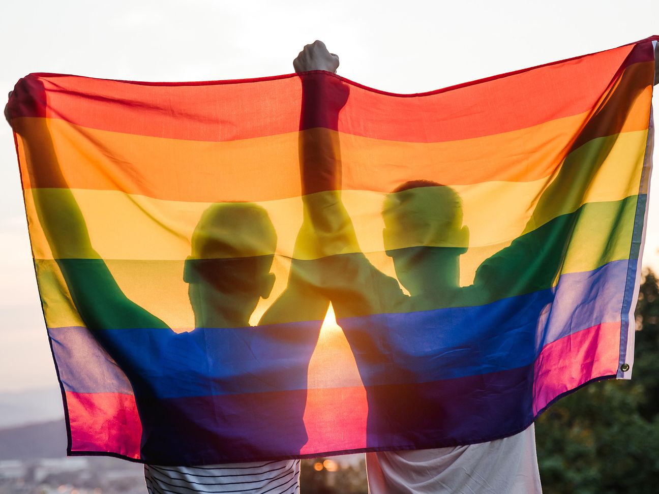 Two people holding a rainbow flag in the air 