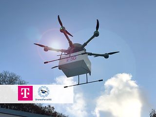 A flying drone in the sky transports a white package with a "T5G" label on it.