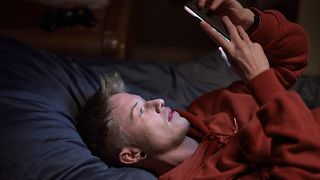 Junger Mann liegt auf dem Bett und schaut in sein Smartphone