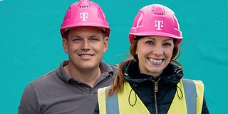 Zwei Personen mit Arbeitskleidung und magenta-farbenen Bauarbeiter-Helm