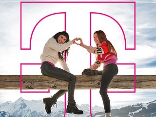 Two young women sit on a beam and form a heart with their hands