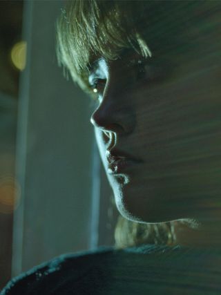 Young woman, depicted from the side, looking out the window, light reflection across the picture.