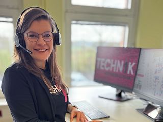  A woman with a headset on her head stands at her standing desk and works