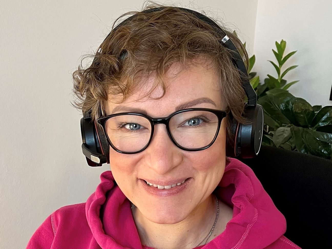 Eine Frau sitzt mit Kopfhörern bei der Arbeit und lächelt in die Kamera
