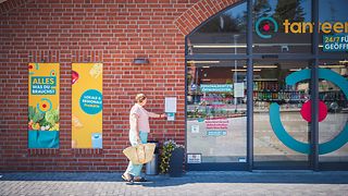Woman with shopping bag opens supermarket door with access card.