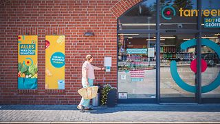 Frau mit Einkaufstasche öffnet Supermarkttür mit Zugangskarte.