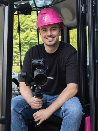 Nick Schneider (Corporate Communications Trainee) sits in the cockpit of a Magenta excavator with his camera equipment.