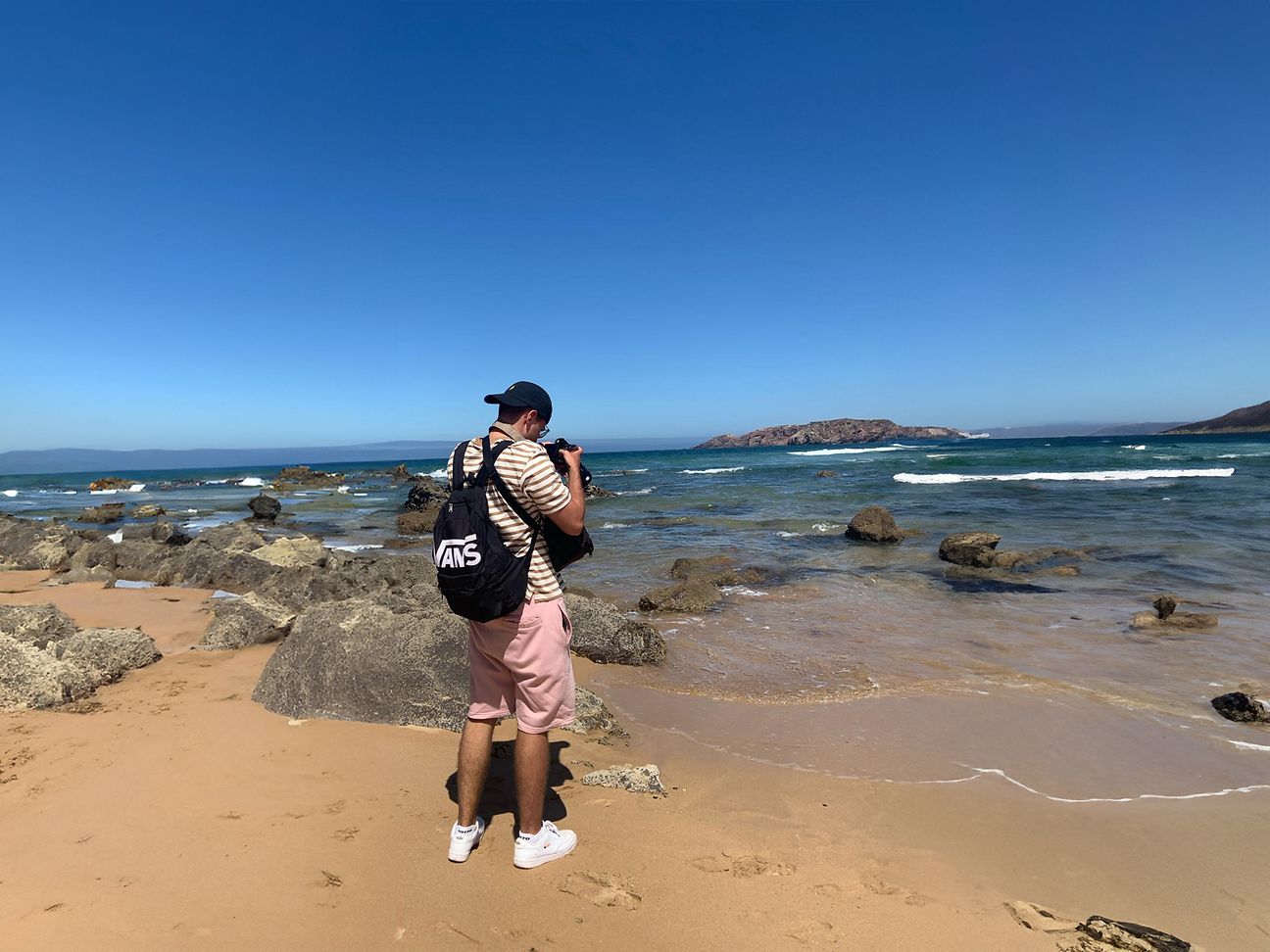 A man stands on the beach in front of the sea and takes photos