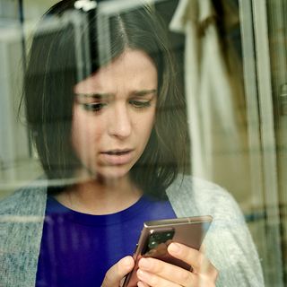 Nachdenkliche junge Frau schaut auf ihr Handy.