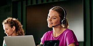 Junge Frau mit Headset sitzt vor dem PC und telefoniert. 