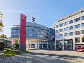 Außenansicht der Telekom Zentrale in Bonn mit magenta-farbenen Fahnen vor dem Eingangsbereich und dem T-Logo auf dem Dach