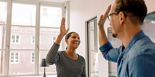 Ein Mann und eine Frau geben sich lachend ein High-Five in einem modernen Büro