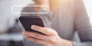 Frau hält ein Handy in der Hand. Darüber ist ein Suchfenster eingeblendet.