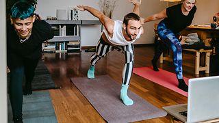 Drei gut gelaunte Personen machen eine Balance-Übung auf Yogamatten. 