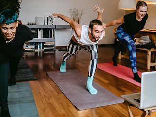 Drei gut gelaunte Personen machen eine Balance-Übung auf Yogamatten. 