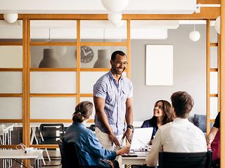 Lächelnder Mann im Gespräch mit Kolleginnen und Kollegen in einem modernen Büro