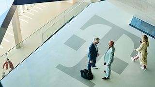 Sicht von oben auf einen weiten Flur mit großem Telekom Logo: Zwei Personen unterhalten sich