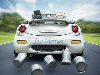 Brautpaar in einem Auto mit angebundenen Blechbüchsen und der Aufschrift "Just married".