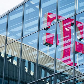 Das große rote Telekom Logo spiegelt sich in der Glasfassade eines modernen Gebäudes