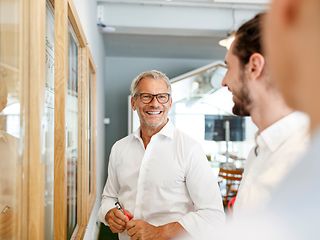 Drei Personen in Businesskleidung unterhalten sich in einem hellen, modernen Büro