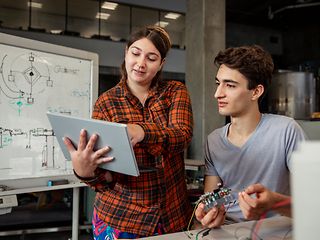 Zwei Personen befinden sich in einem Tech-Labor, sie halten einen Mini-Computer und ein Tablet in der Hand