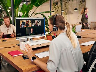 Eine Frau mit Headset nimmt an einem Online-Meeting teil, auf Ihrem Bildschirm sind drei weitere Teilnehmende zu sehen