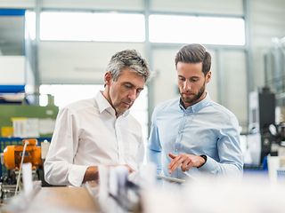 Zwei Männer in einem modernen Büro mit Blick auf ein Tablet 