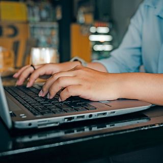 Hände tippen auf der Tastatur eines Laptops.