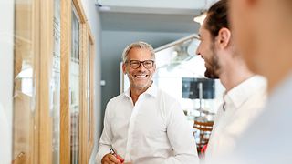 Drei Personen in Businesskleidung unterhalten sich in einem hellen, modernen Büro