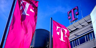 Blick auf ein Telekom Gebäude mit großem Telekom Logo und magentafarbenen Fahnen vor blauem Himmel