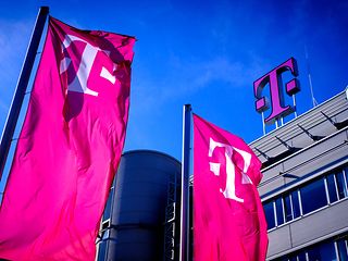 Blick auf ein Telekom Gebäude mit großem Telekom Logo und magentafarbenen Fahnen vor blauem Himmel