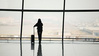 A person with a suitcase stands at a large window in the airport and looks at the runway