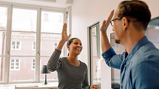 A man and a woman smile and give each other a high-five in a modern office