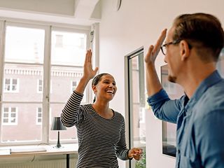 A man and a woman smile and give each other a high-five in a modern office