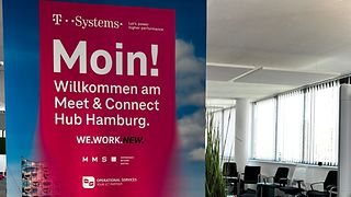 Ein magenta Banner mit der Elbphilharmonie Hamburg als Hintergrund, steht am Eingang eines Konferenzraumes.