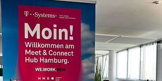 Ein magenta Banner mit der Elbphilharmonie Hamburg als Hintergrund, steht am Eingang eines Konferenzraumes.