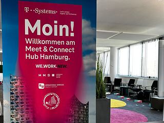 Ein magenta Banner mit der Elbphilharmonie Hamburg als Hintergrund, steht am Eingang eines Konferenzraumes.