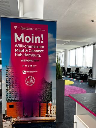 Ein magenta Banner mit der Elbphilharmonie Hamburg als Hintergrund, steht am Eingang eines Konferenzraumes.