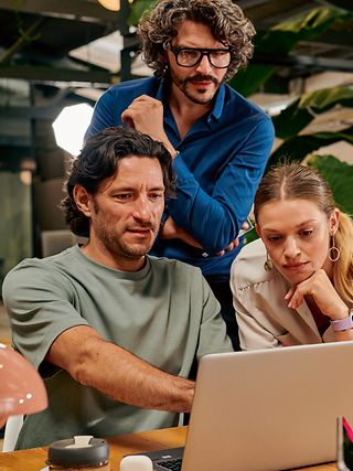 Two men and a woman are standing together at a table and discussing things with each other.