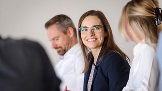 Several people sitting as a table, one woman wearing glasses smiling at another