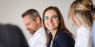 Several people sitting as a table, one woman wearing glasses smiling at another