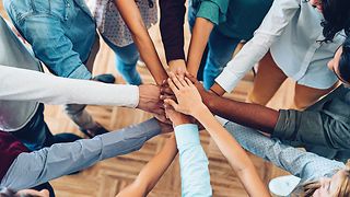 View from above: A group of people stand in a circle and hold their hands over each other as a team