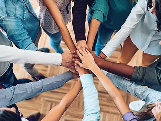 View from above: A group of people stand in a circle and hold their hands over each other as a team