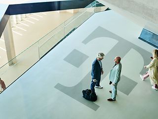 View from above of a wide corridor with a large Deutsche Telekom logo: Two people are talking