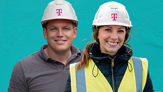 Man and woman wearing pink construction helmets with the Deutsche Telekom logo and smiling into the camera