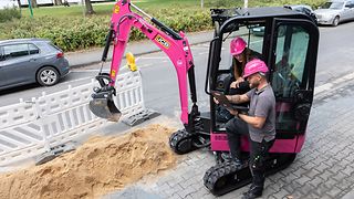 Magenta digger excavating a narrow trench next to a road to lay fiber-optic cable.