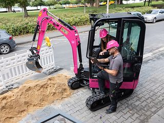 Magenta digger excavating a narrow trench next to a road to lay fiber-optic cable.