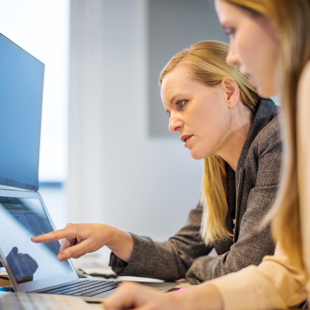 A woman explains something to another on a laptop in an office